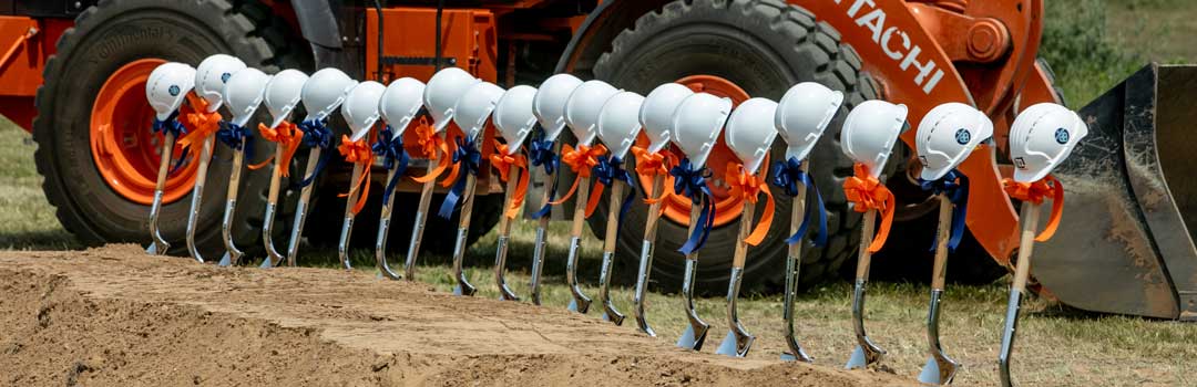 Shovels lined up in dirt topped with hardhats
