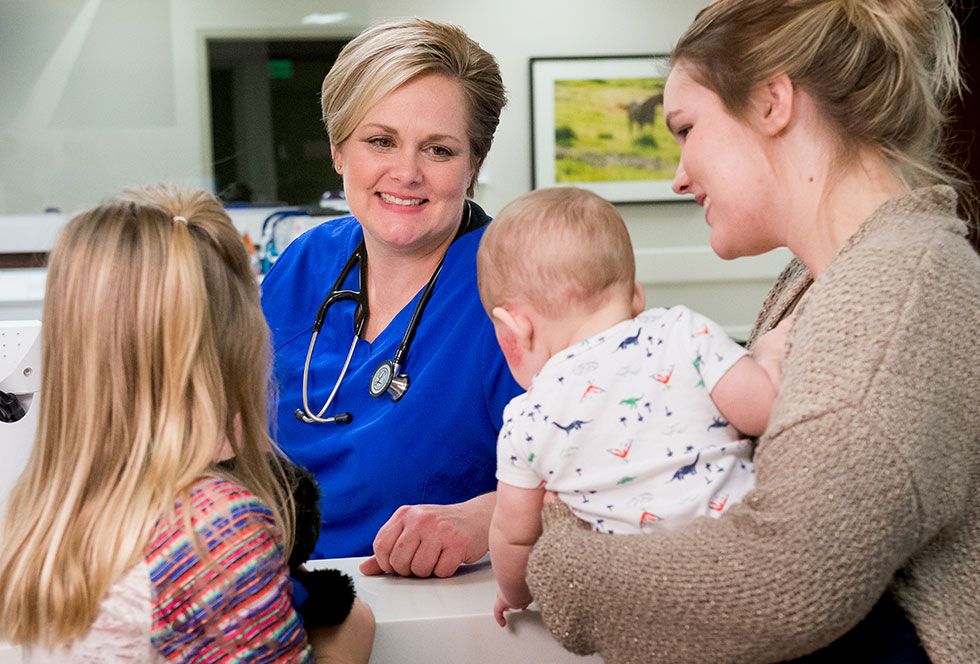  A woman with a stethoscope engages in conversation with a baby and two women, showcasing a caring medical environment.