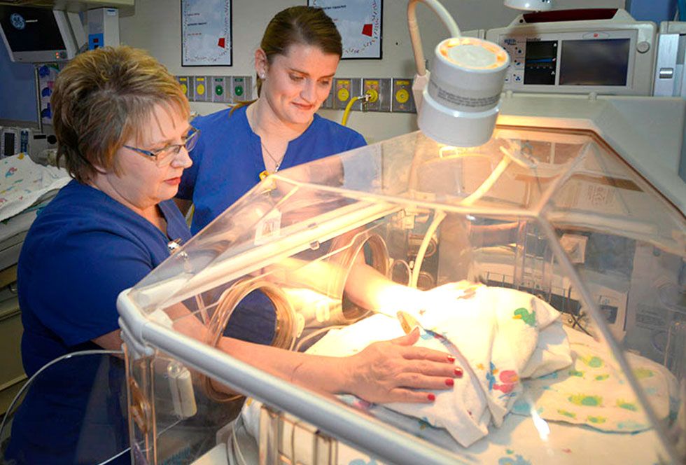 Two nurses attentively caring for a newborn in an incubator, ensuring a safe and nurturing environment for the baby.